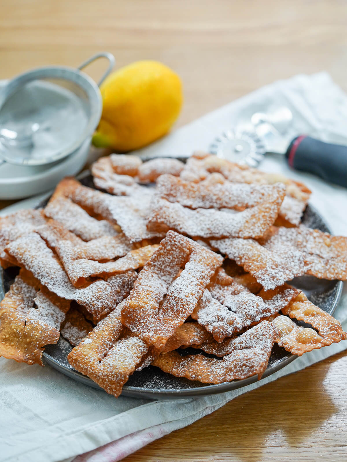 side view of chiacchiere fried pastries with lemon behind plate.