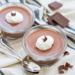 dishes of chocolate panna cotta with spoons in front and hunks of chocolate behind.