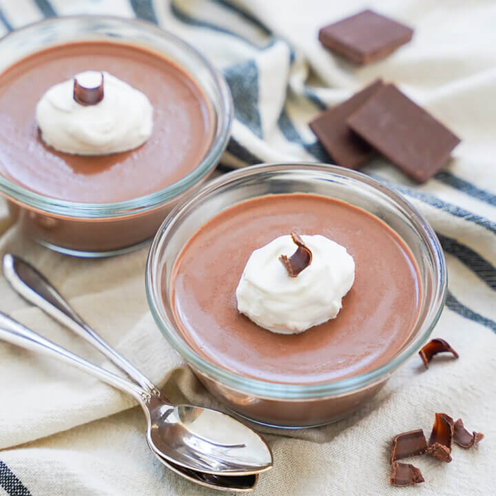 dishes of chocolate panna cotta with spoons in front and hunks of chocolate behind.
