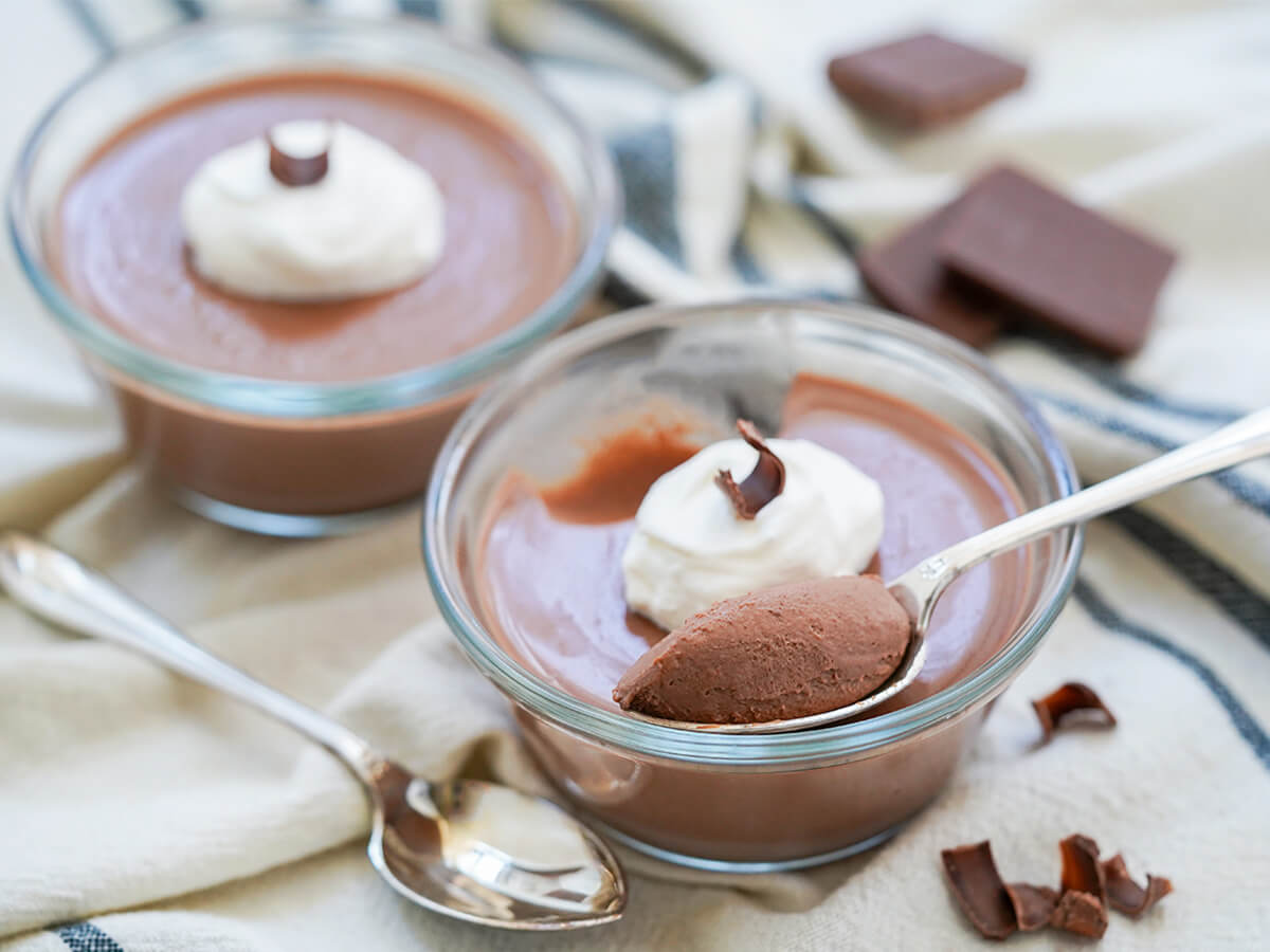two dishes of chocolate panna cotta with spoonful resting on one in front.