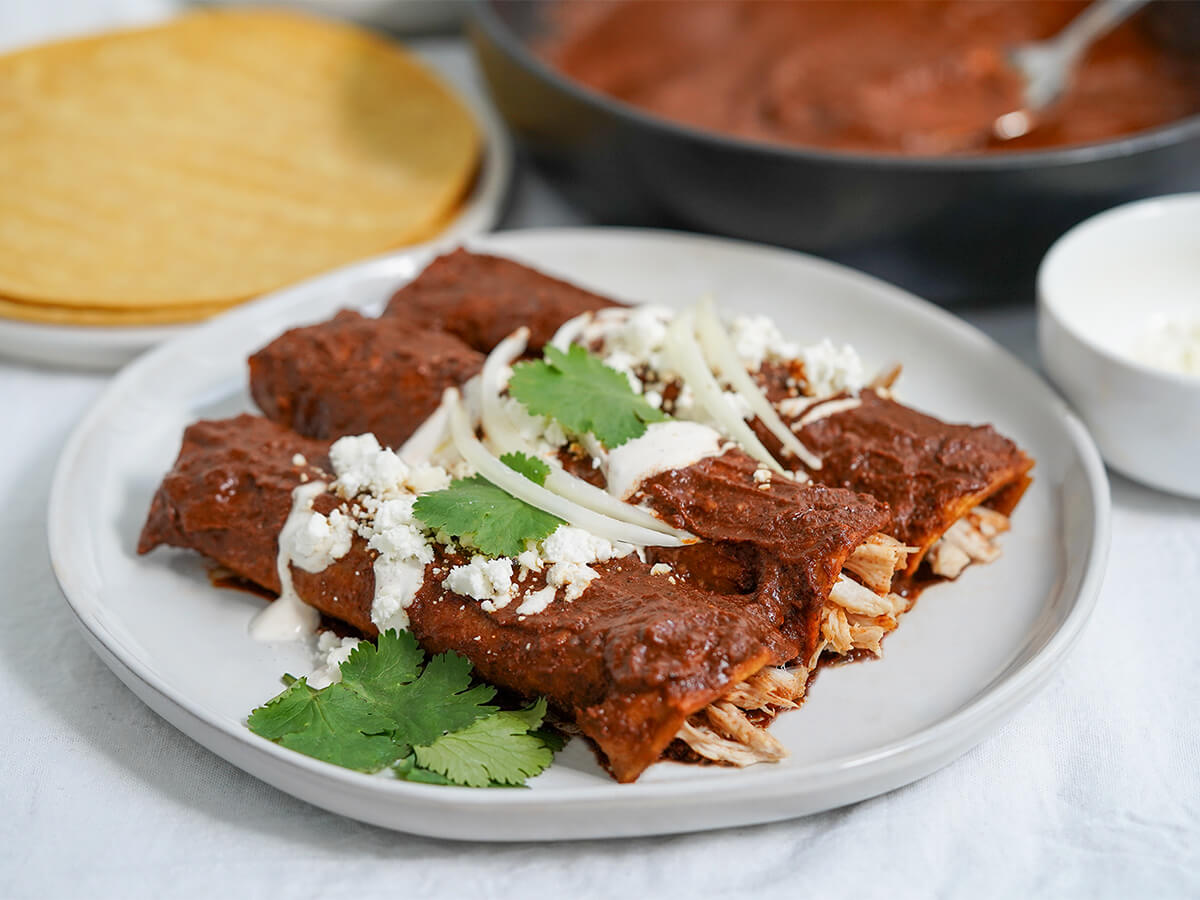 plate of enmoladas, chicken mole enchiladas three chicken-filled enmoladas on a plate viewed from side.
