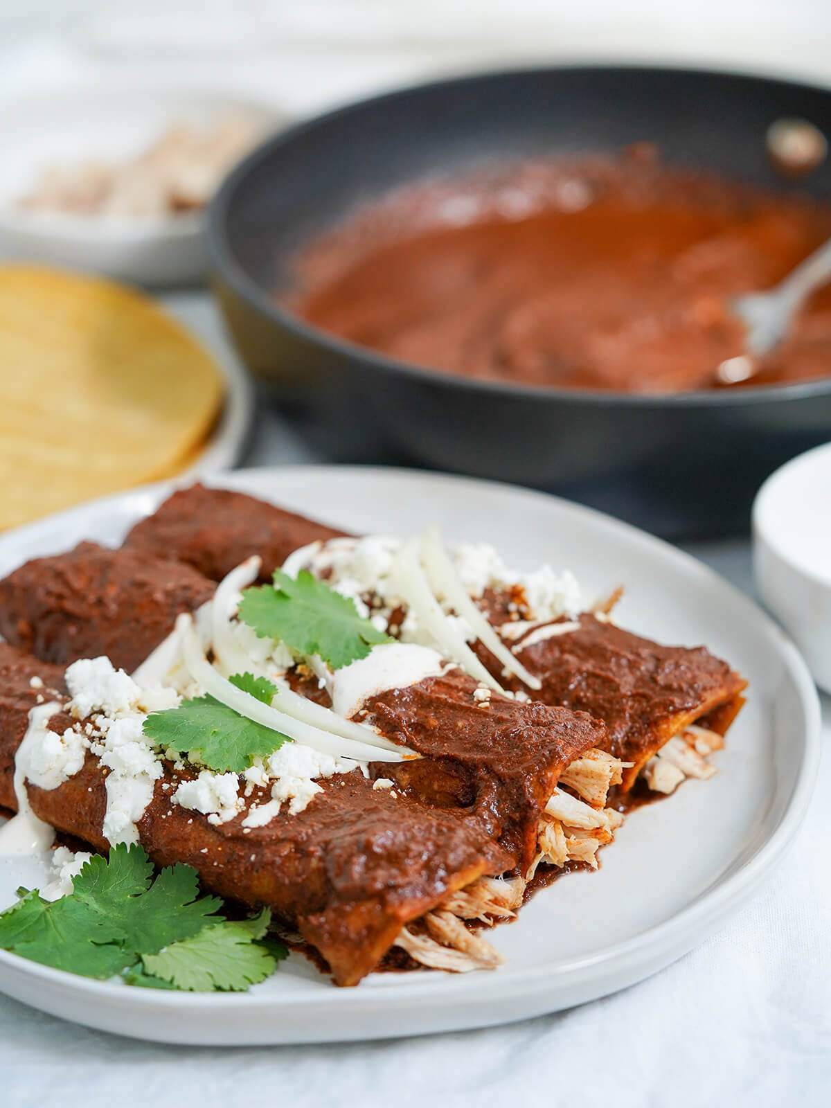 Enmoladas combine fried corn tortillas, mole sauce and shredded chicken for a wonderfully quick, easy and tasty Mexican meal. These chicken mole enchiladas are comforting and perfect any excuse. three enmoladas from side with skillet of mole blurred behind.