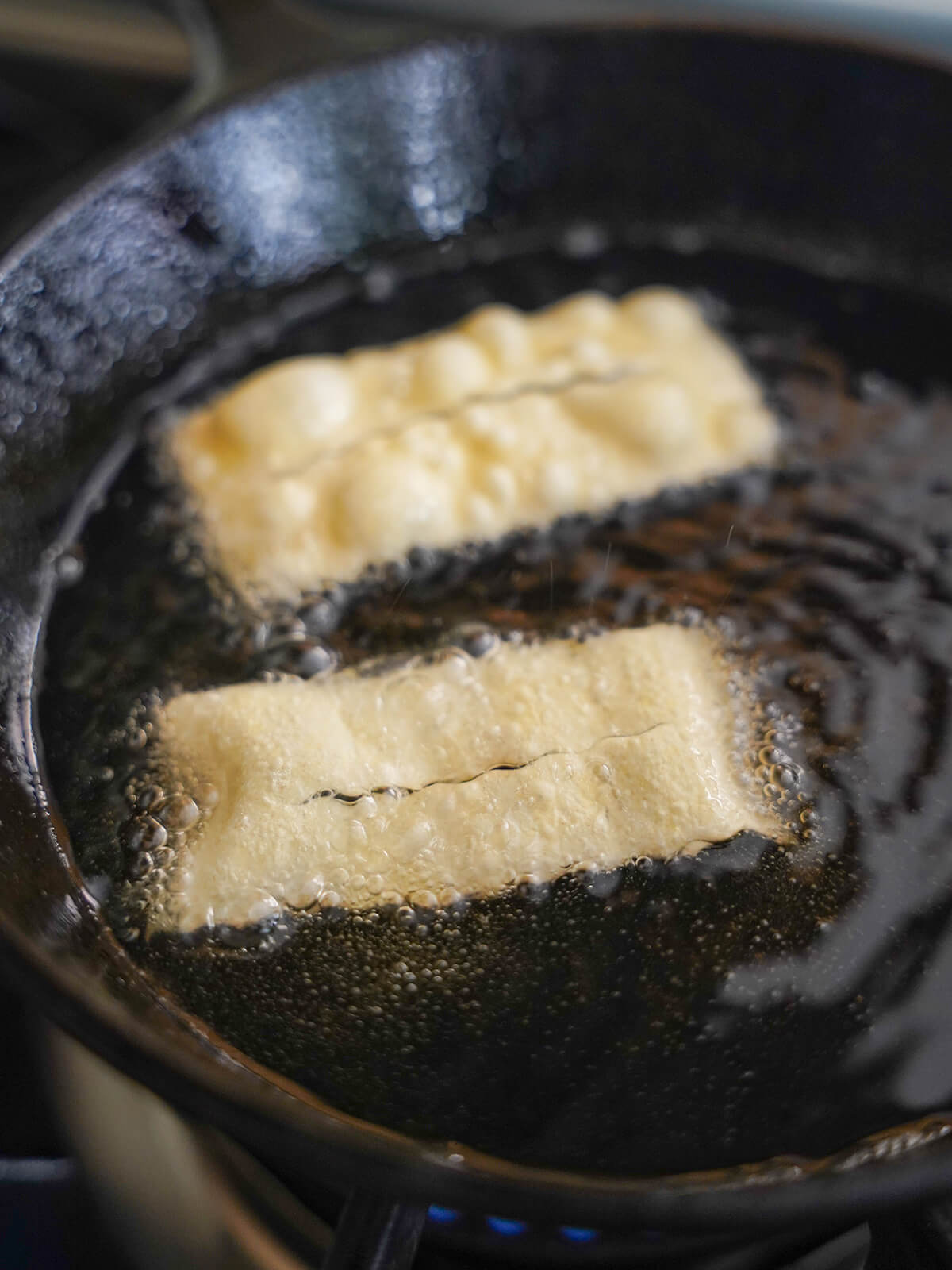 frying chiacchiere fried pastries in skillet of oil with bubbles around the pieces of dough.