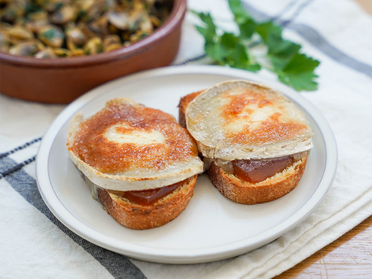 two slices of goat cheese toast on small plate with mushrooms and parsley blurred in background.