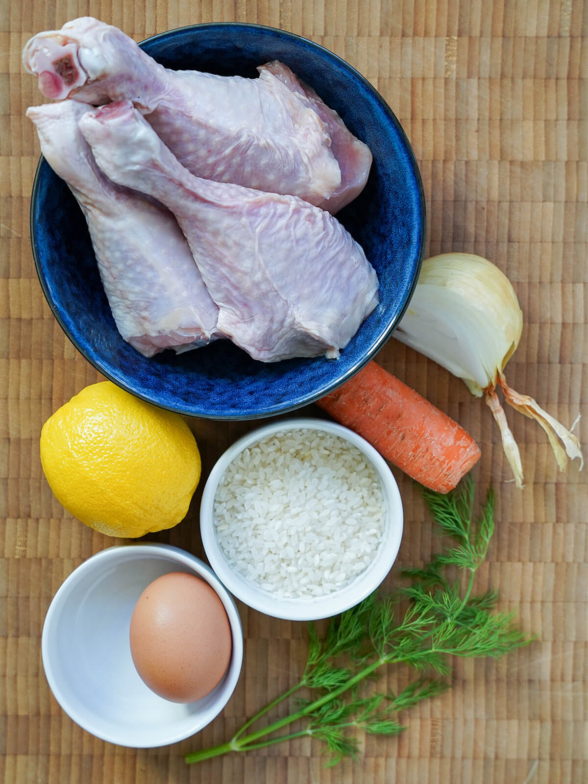 bowl of chicken thighs, carrot, onion, dill, rice, egg and lemon on wooden board.