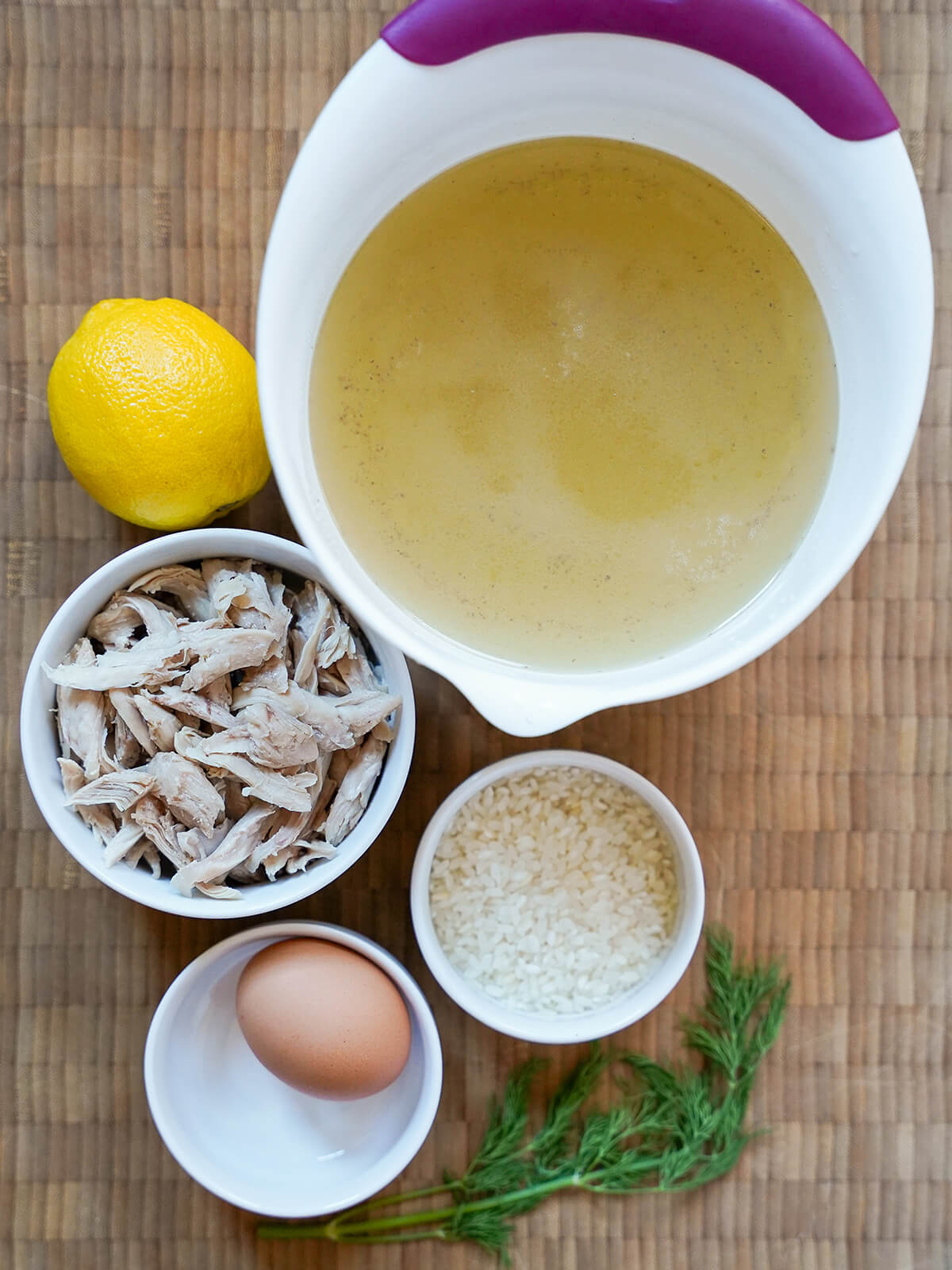 bowls of chicken stock, shredded chicken, rice, an egg with dill and lemon to side.
