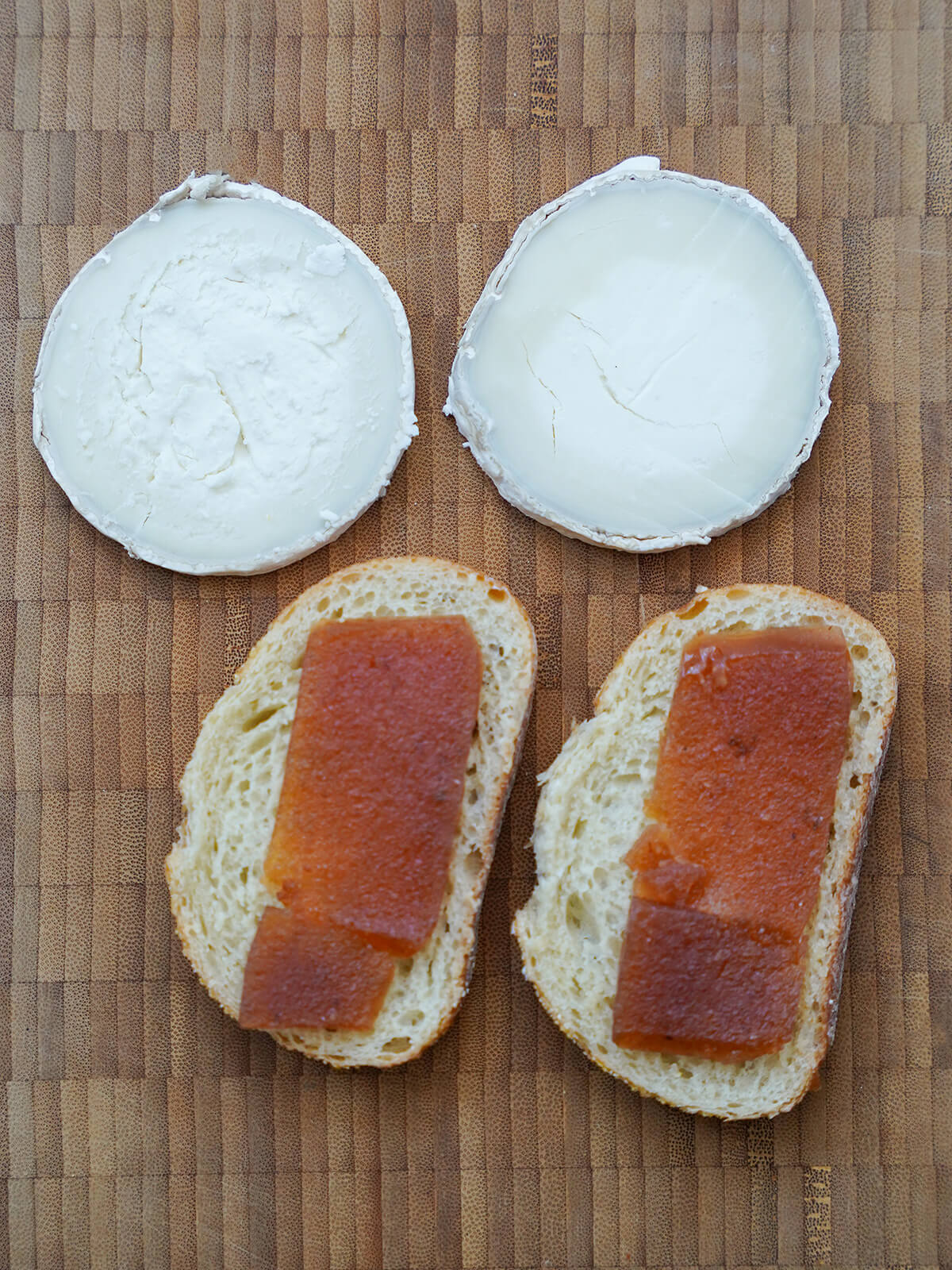 pieces of bread with slices of membrillo on top and slices of goat cheese above on board.