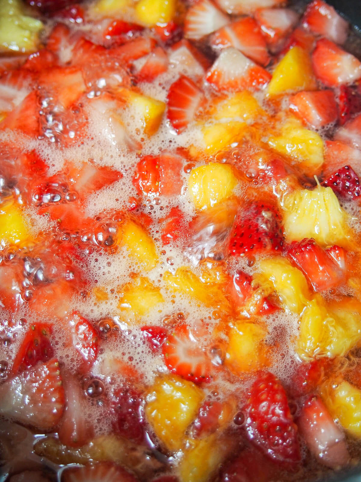 simmering chunks of strawberries and peaches in pot.