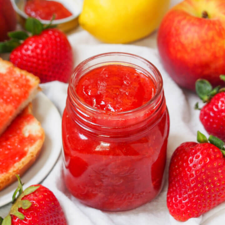 jar of strawberry peach jam with fruit all around it.