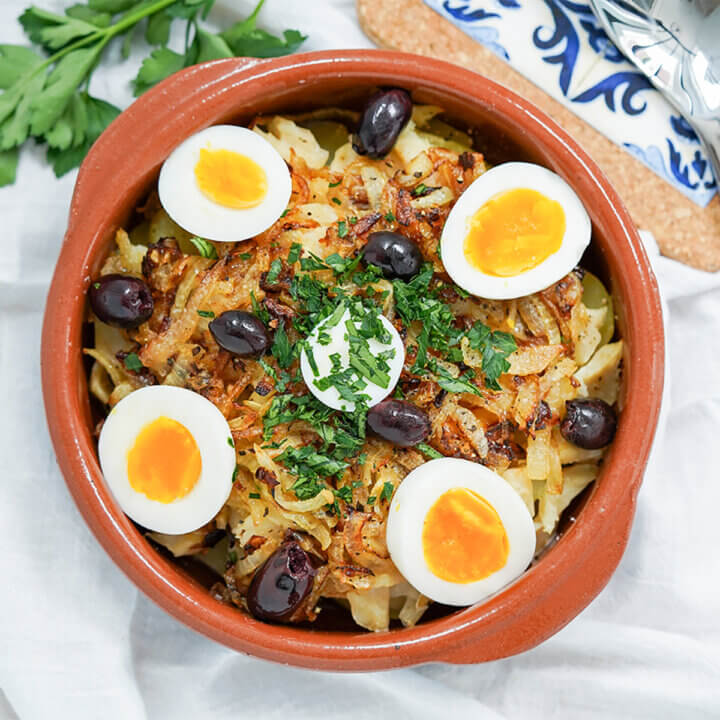 dish of Bacalhau à Gomes de Sá, Portuguese salt cod, from overhead topped with olives and egg.