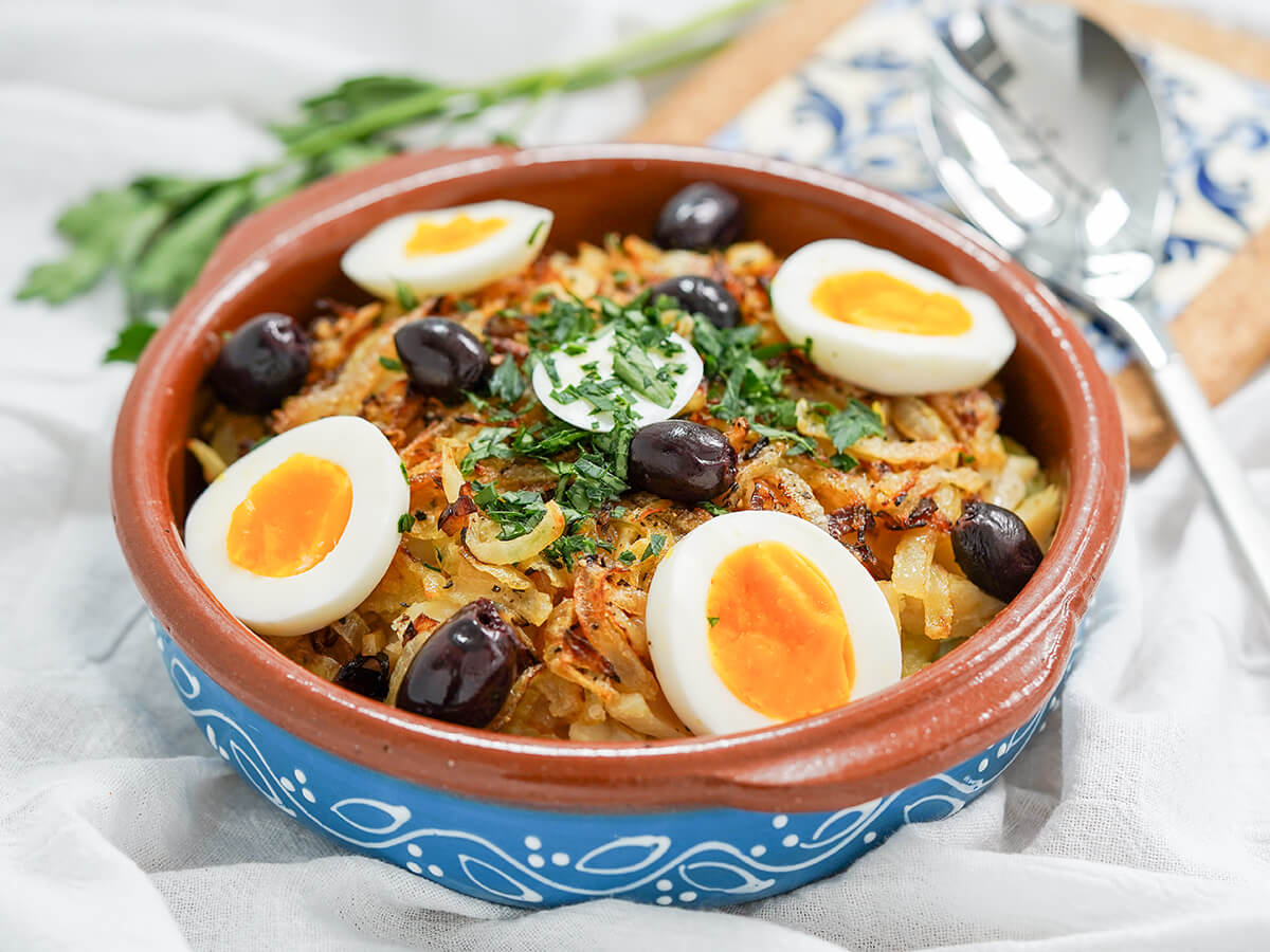 side view of dish of Bacalhau à Gomes de Sá, Portuguese salt cod topped with egg and olives.