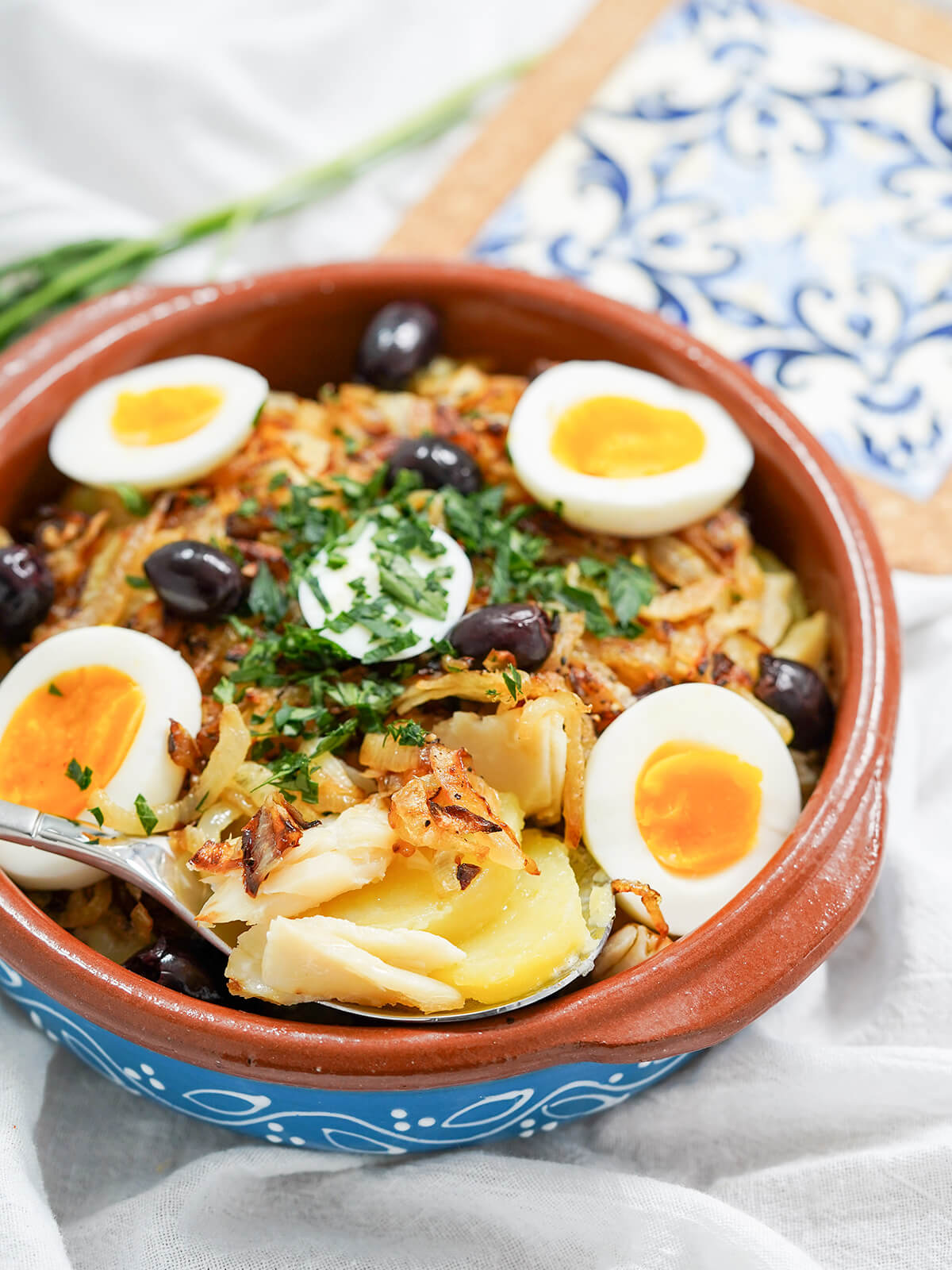 spoonful at front of dish of Bacalhau à Gomes de Sá, Portuguese salt cod, showing cod and slices of potato.