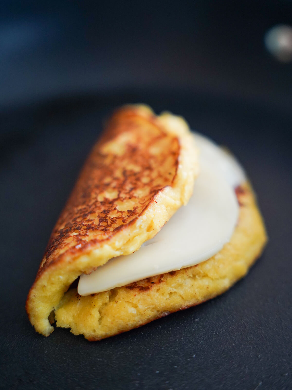 folded over cachapa in skillet with cheese slice in middle