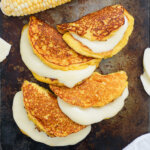 close view of four cachapas, Venezuelan corn pancakes with cheese oozing from them.