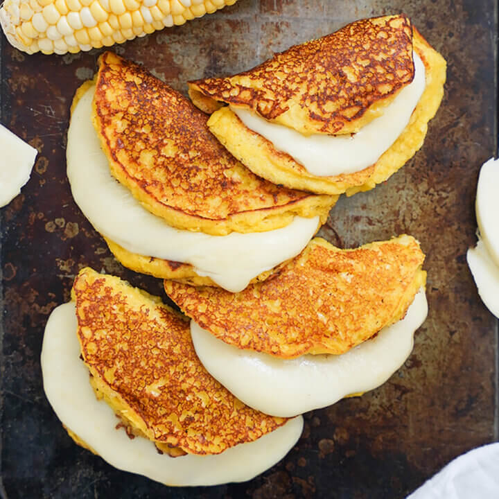 close view of four cachapas, Venezuelan corn pancakes with cheese oozing from them.