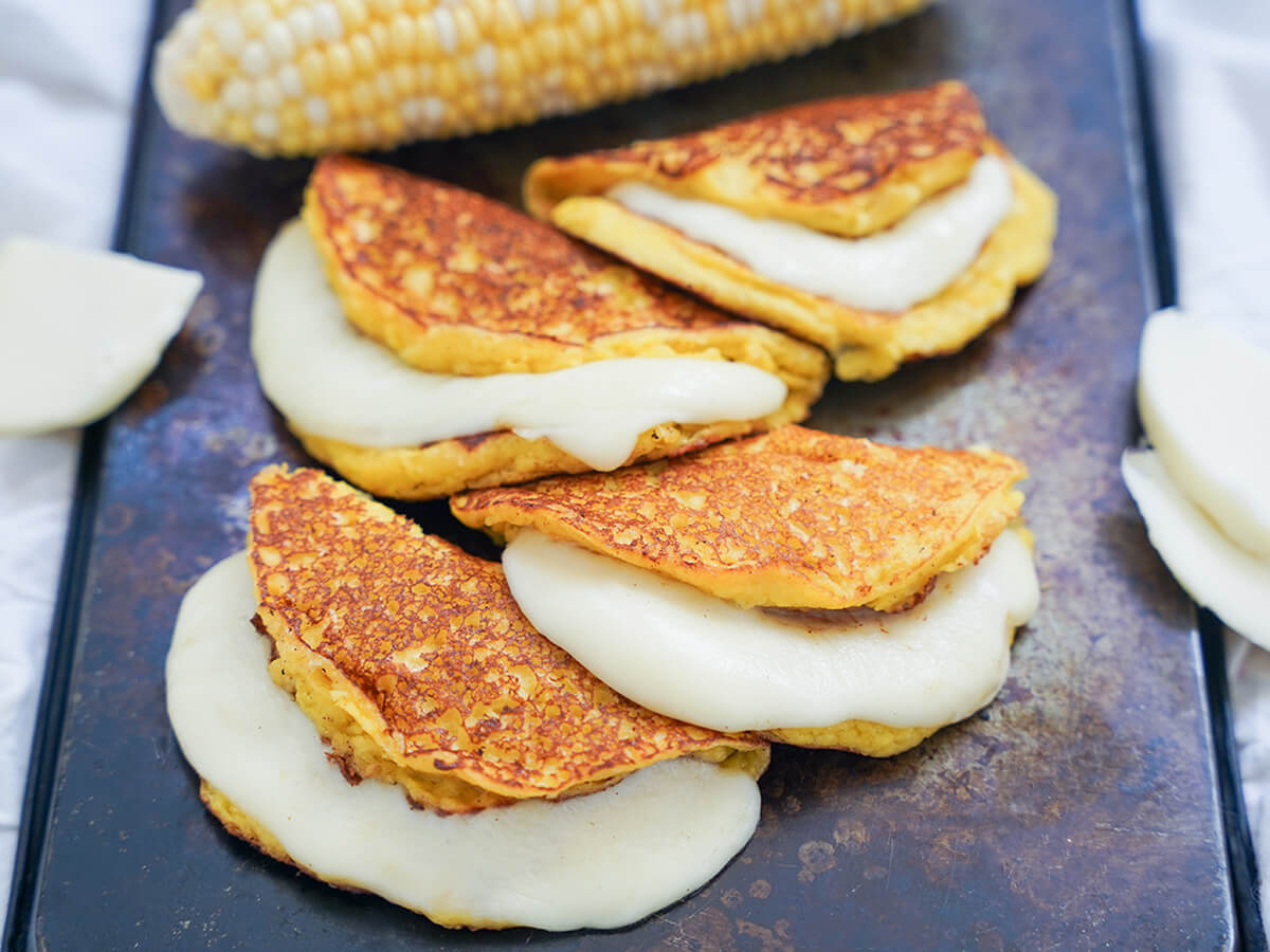 four cachapas, Venezuelan corn pancakes, overlapping each other on a tray.