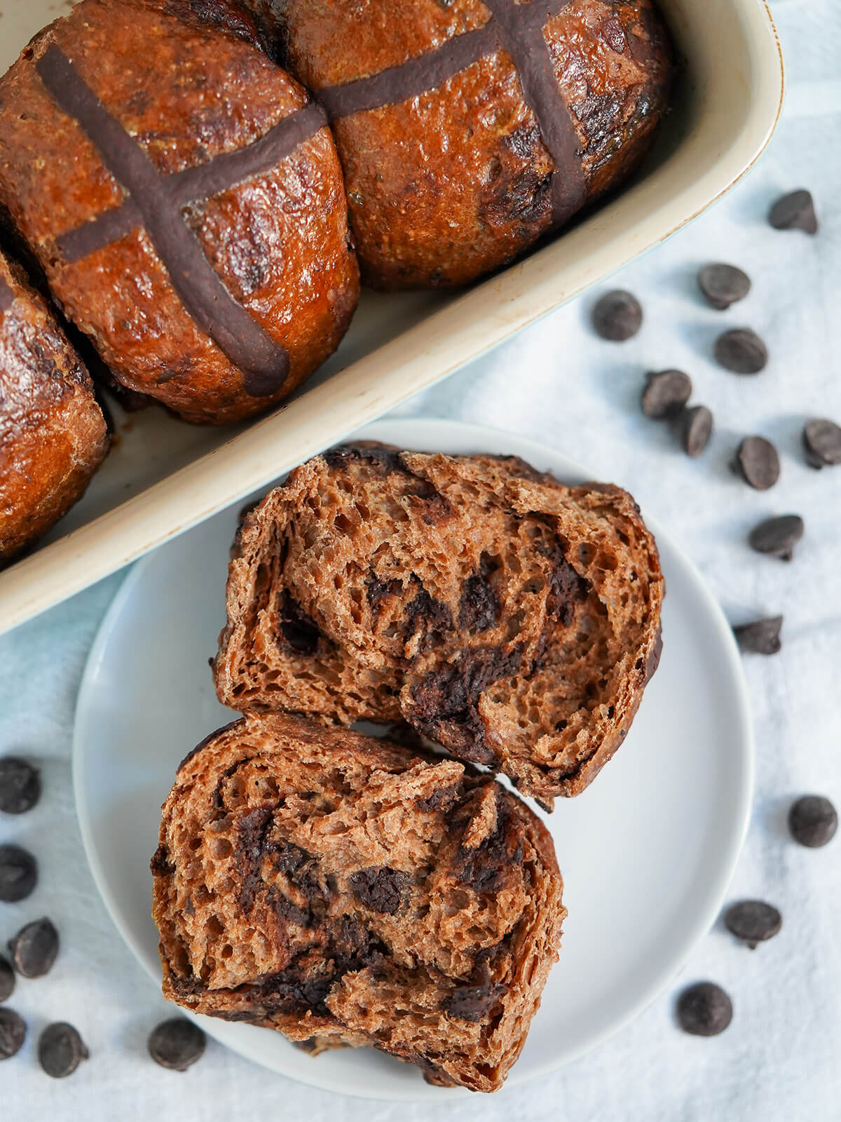 overhead view of a split open chocolate hot cross bun with chocolate chips around plate.