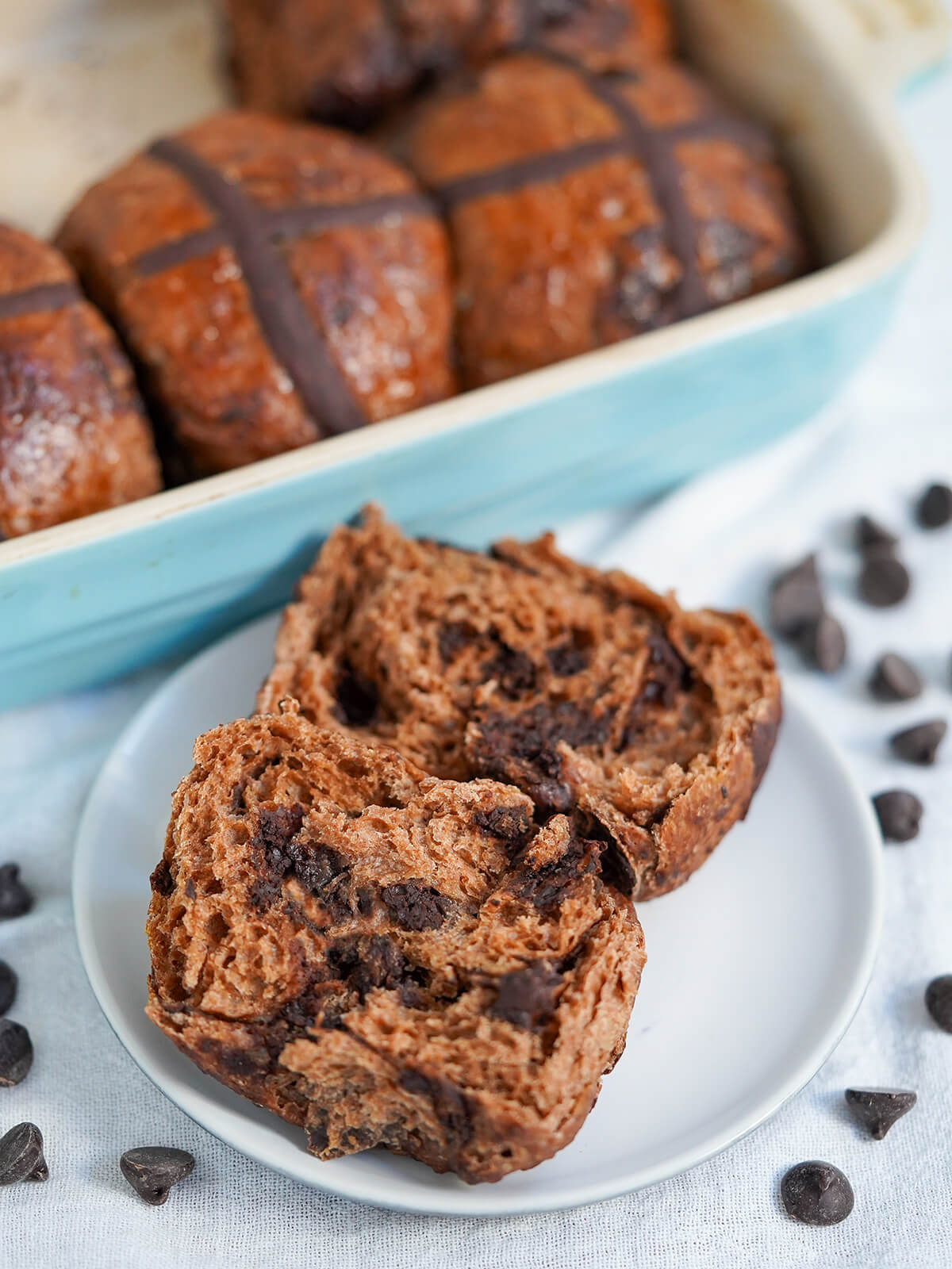 a split open chocolate hot cross bun on a plate with more behind.