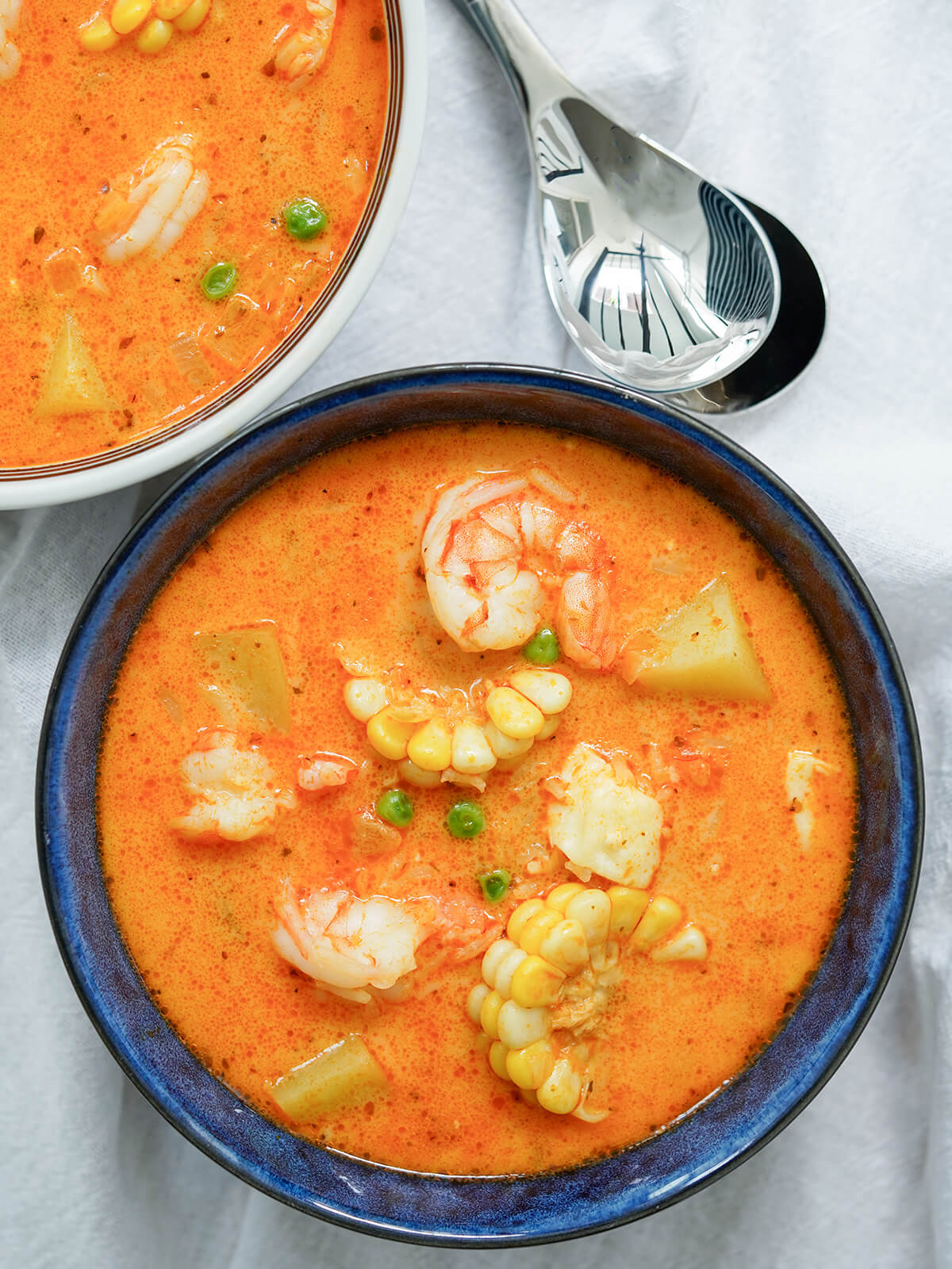 overhead view of bowl of chupe de camarones, Peruvian shrimp chowder with spoons above.