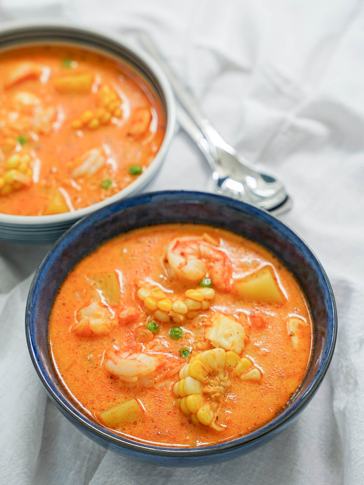 bowl of chupe de camarones, Peruvian shrimp chowder with part view of another bowl behind and spoons to side.