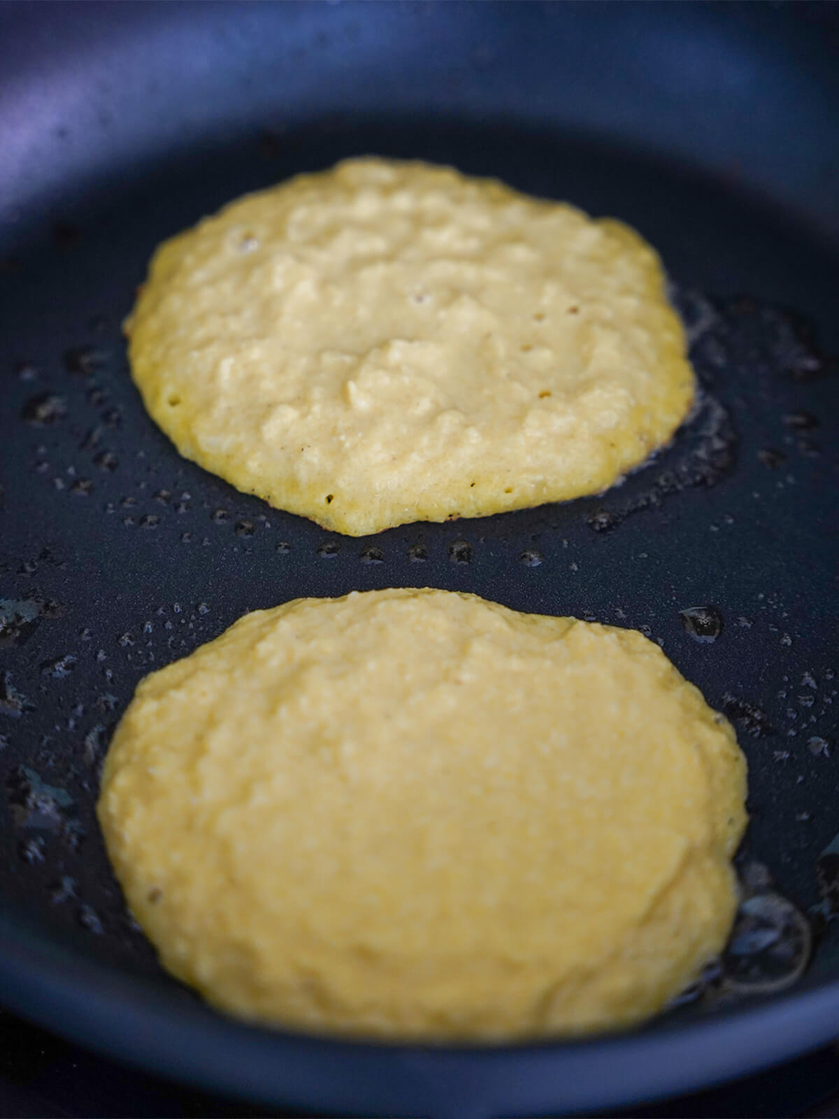 batter for two cachapas, Venezuelan corn pancakes, cooking in skillet.