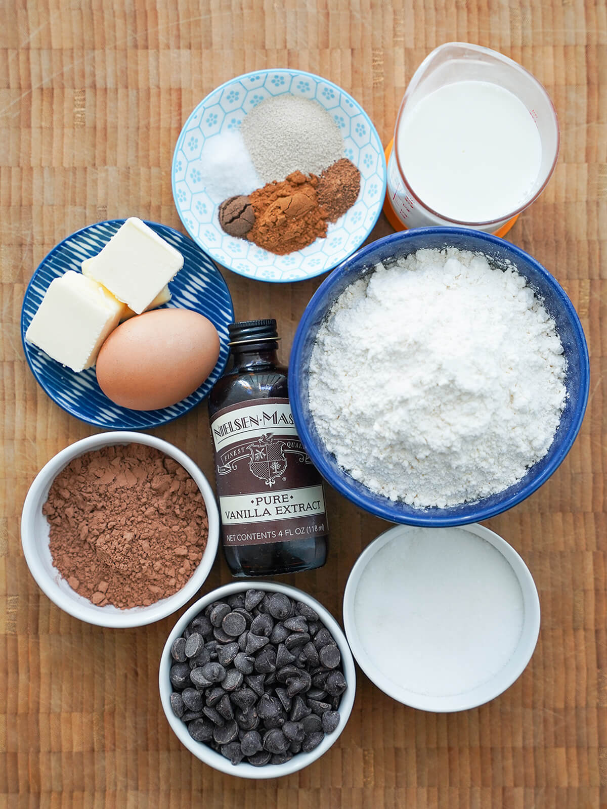 bowls of flour, cocoa powder, chocolate chips, sugar and small plates with butter, egg, spices and measure with milk.