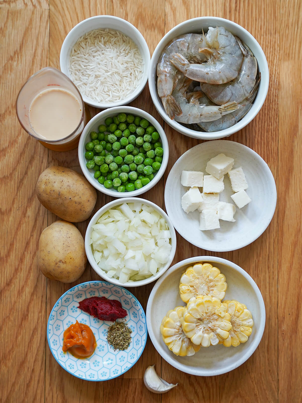 bowls with shrimp, rice, peas, onion, slices of corn cob, cheese cubes and pastes with potatoes to side.