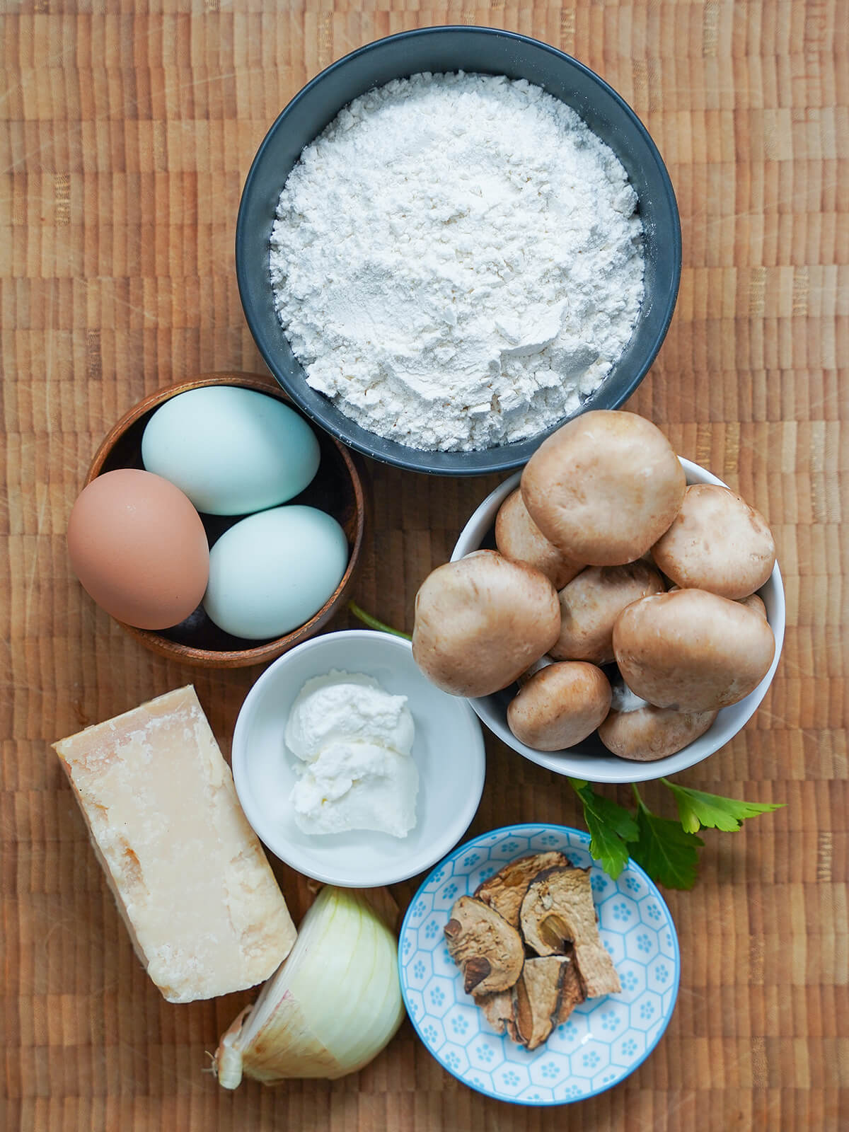 bowls of flour, mushrooms, eggs, ricotta, dried porcini with onion and parmesan to side.