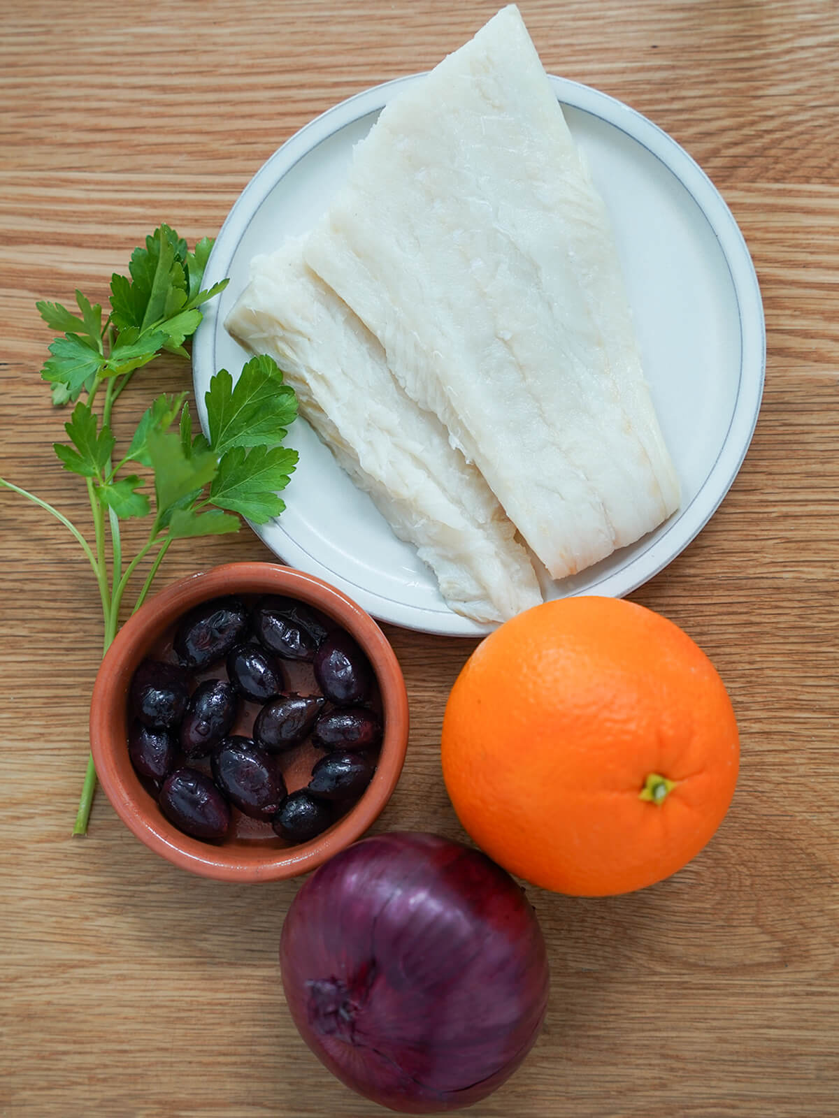 plate with salt cod, orange, dish of black olives, red onion and sprig parsley.