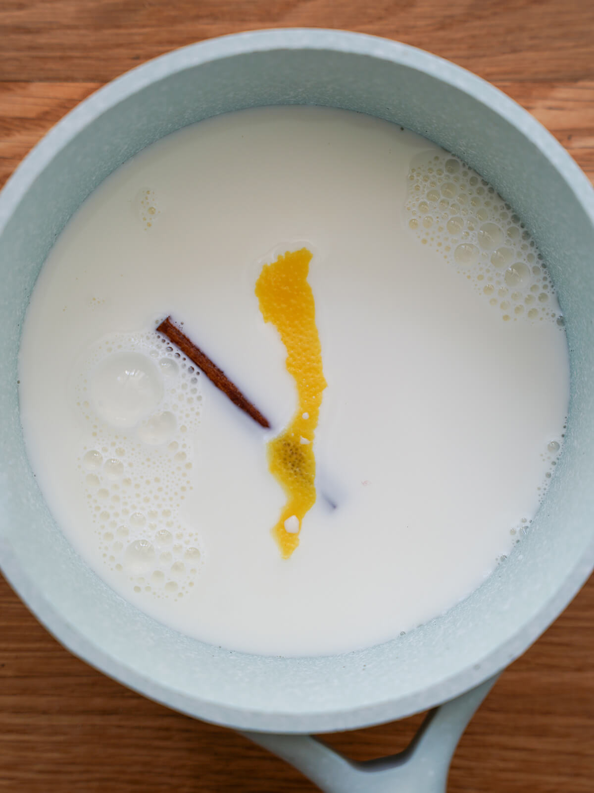pan of milk with cinnamon stick and lemon peel floating in top.