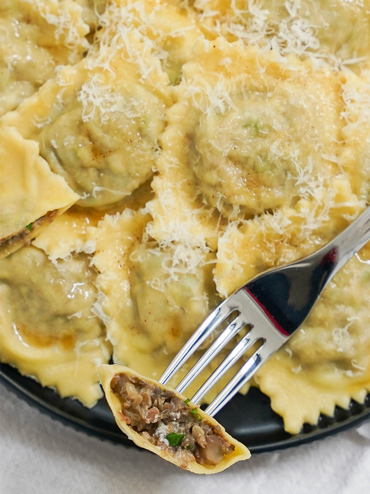 close view of cut open mushroom ravioli on fork over plate with more ravioli.