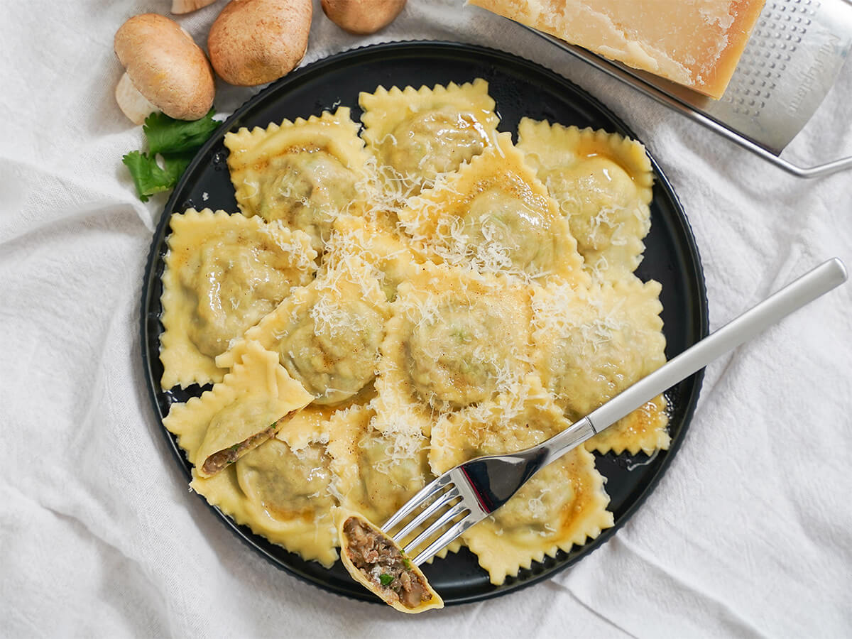 plate of mushroom ravioli with fork of part of a ravioli resting on top.