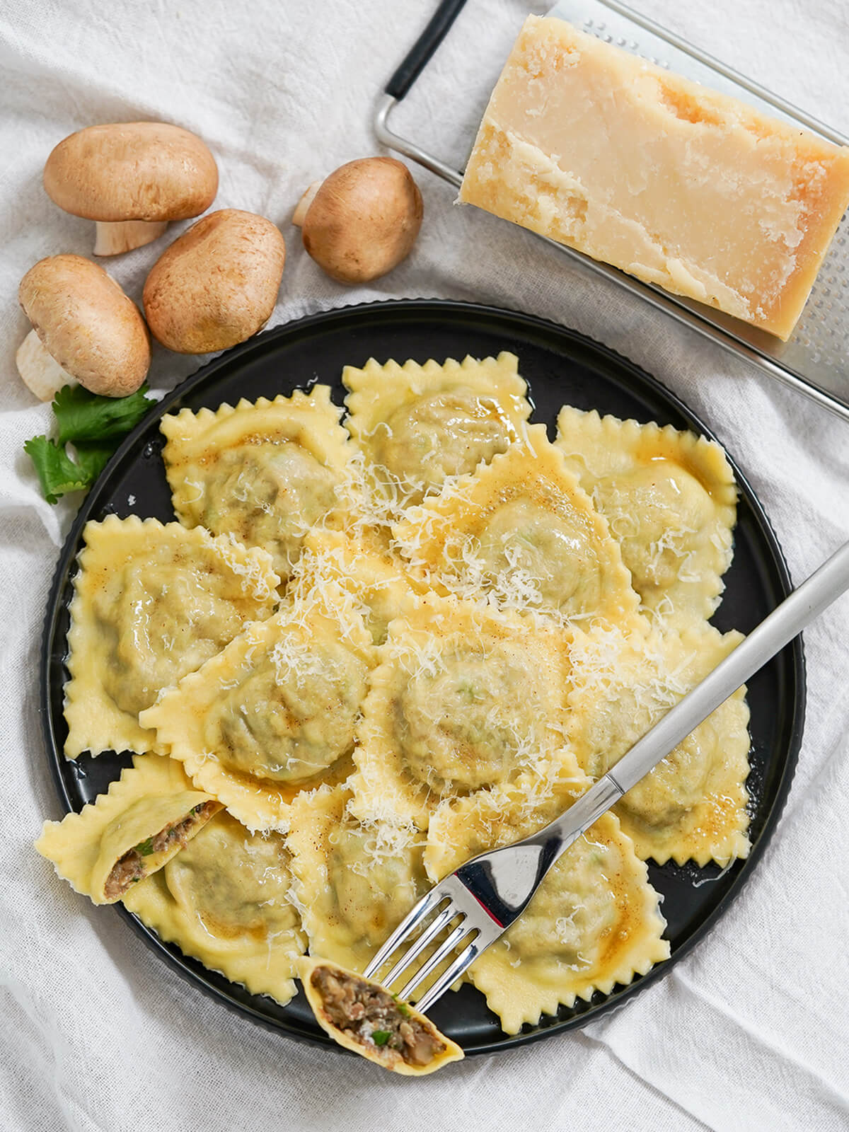 plate of mushroom ravioli with block of parmesan and some mushrooms above plate.