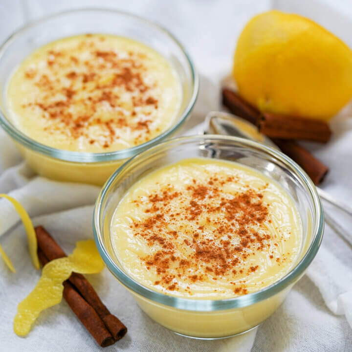 two dishes of natillas, Spanish custard, with lemon and cinnamon sticks behind and to side.