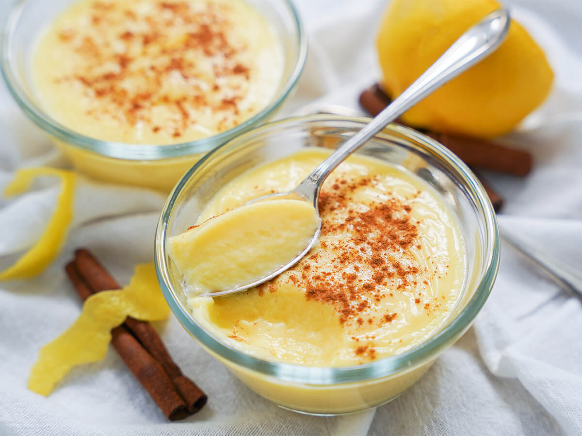 dish of natillas, Spanish custard with spoon resting on top and cinnamon stick and lemon peel to side.