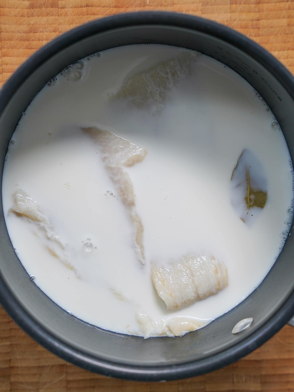 pieces of salt cod in pot with milk and bay leaf to side.