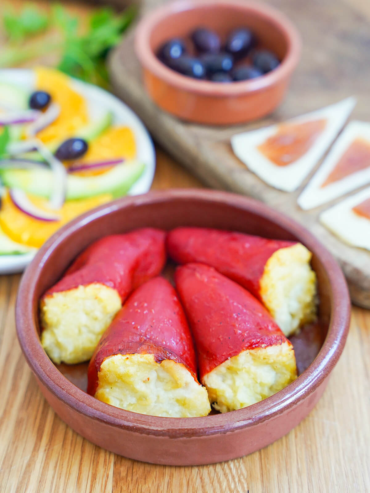 dish of salt cod stuffed piquillo peppers with salad, cheese and olives blurred in background.