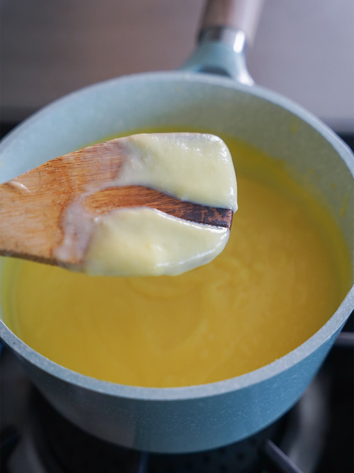 spoon with some custard on it with line scraped to show thickness held over pot.