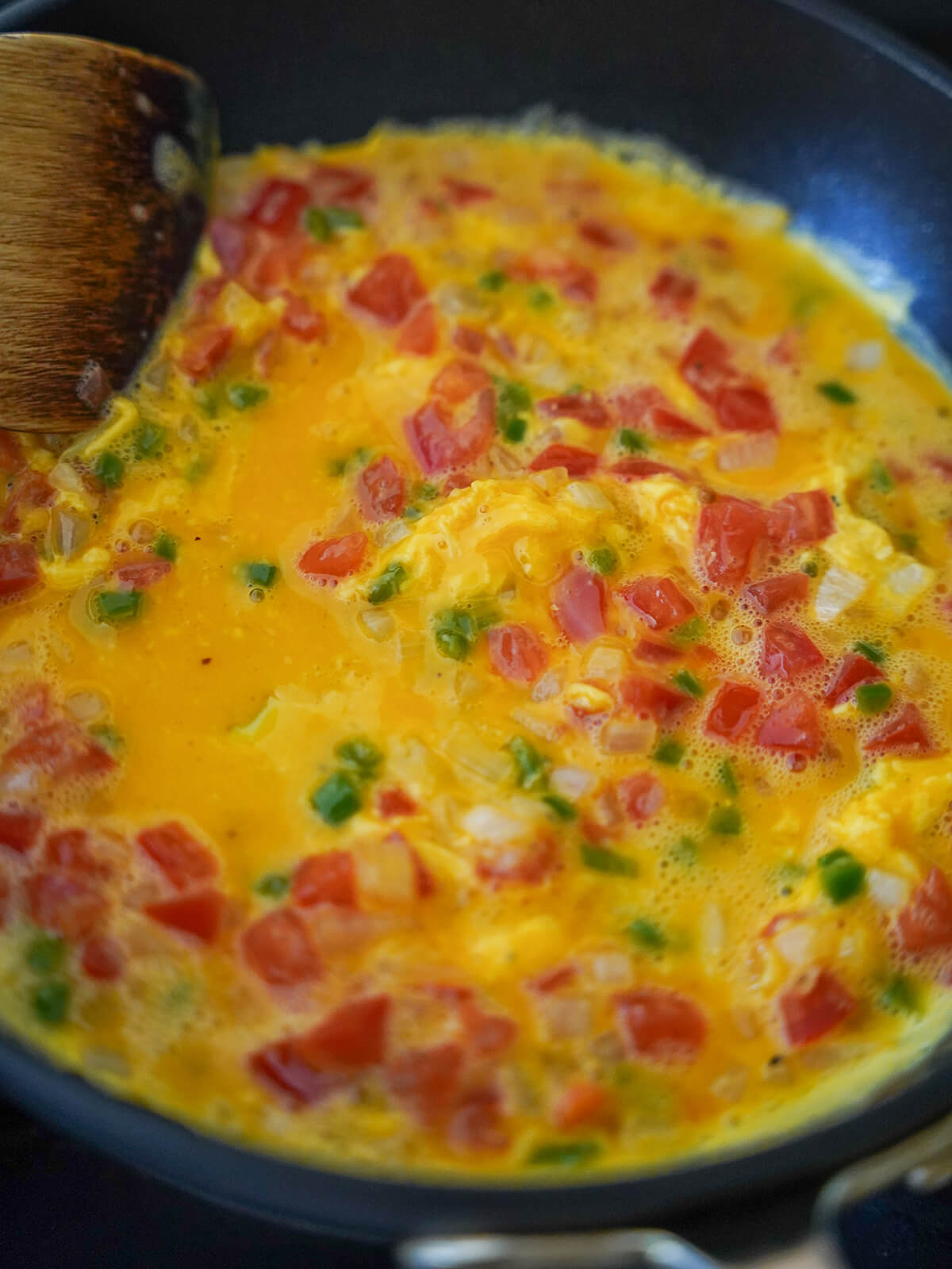 egg cooking in skillet with dots of tomato, jalapeno and onion dotted through.