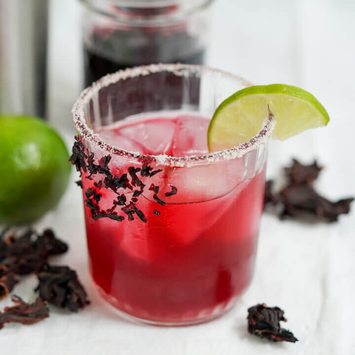 glass of hibiscus margarita with a slice of lime on top of glass.