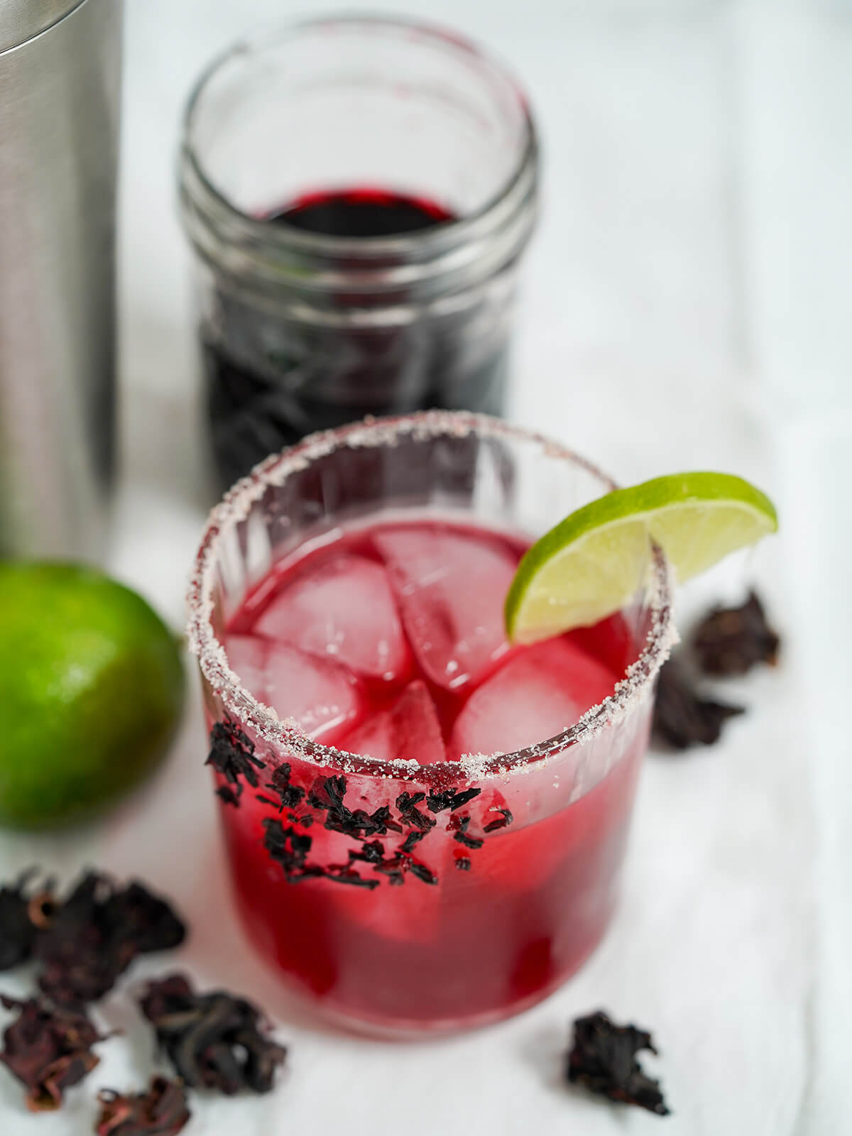glass of hibiscus margarita with a salt rim and some cut hibiscus flowers on side of glass.