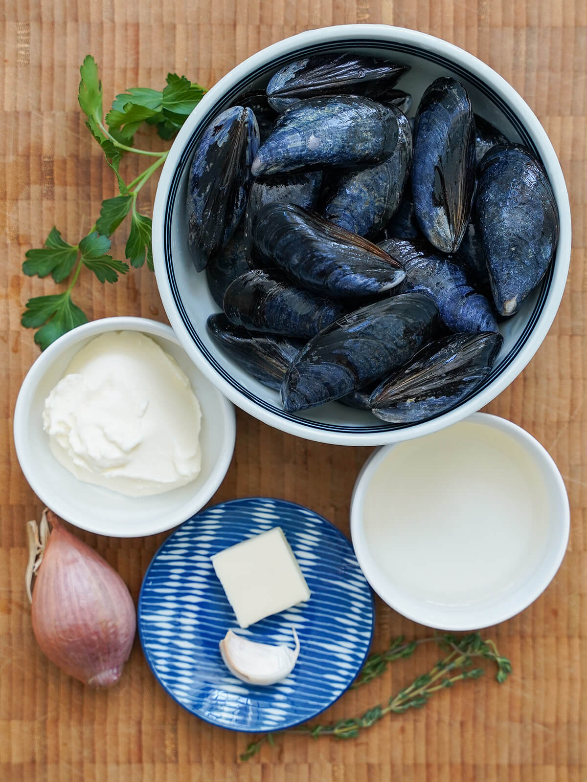 ingredients for mussels in cream bowls of mussels, cream, wine, butter, garlic with shallot, sprigs of thyme and parsely around.