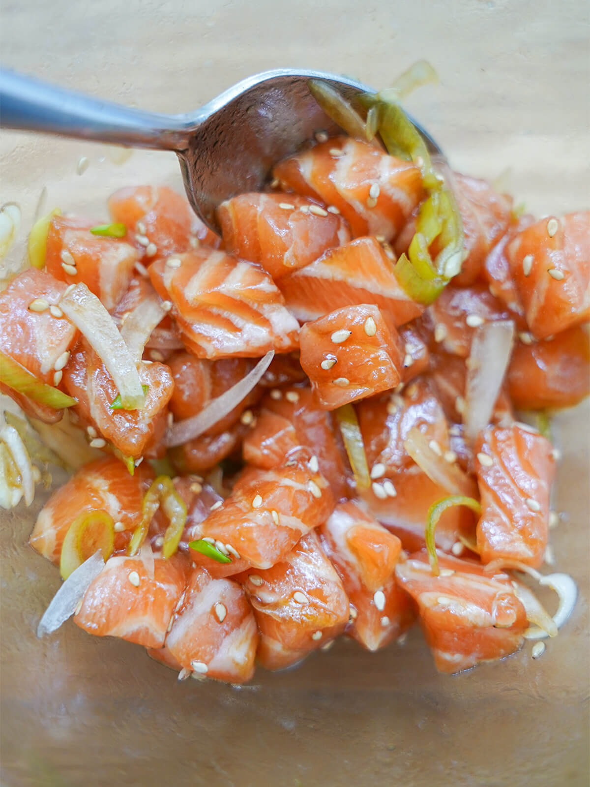 mixing cubes of salmon with sliced onion and green onion, sesame seeds and soy dressing.