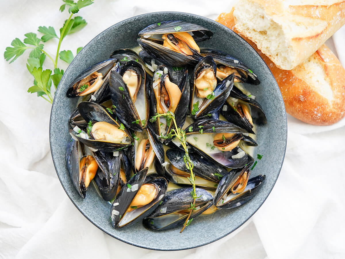 bowl of mussels in cream bowl of mussels in cream with chunks of baguette above bowl.