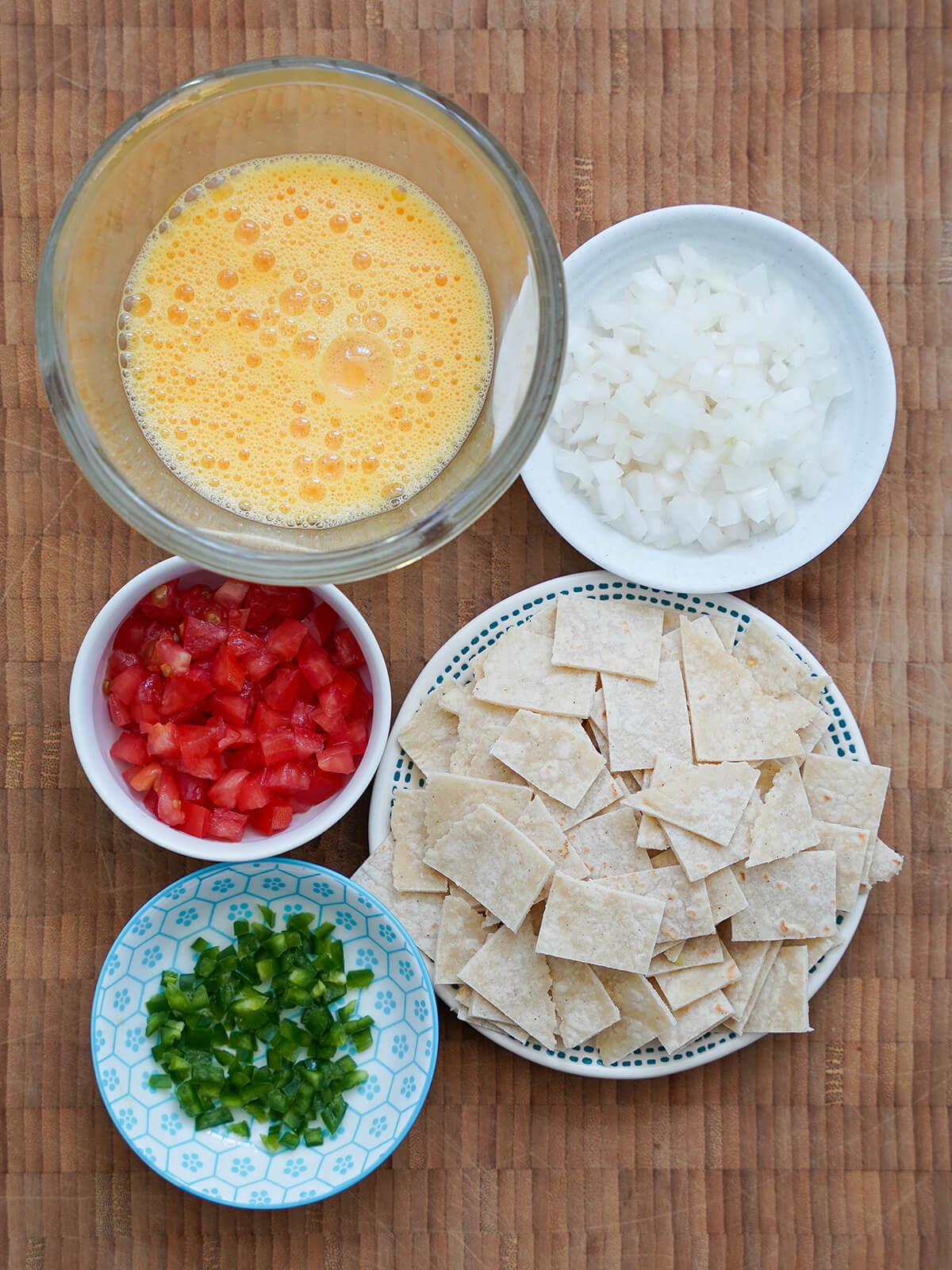 bowls of beated egg, chopped onion, tomato, jalapeno and plate of diced tortillas.