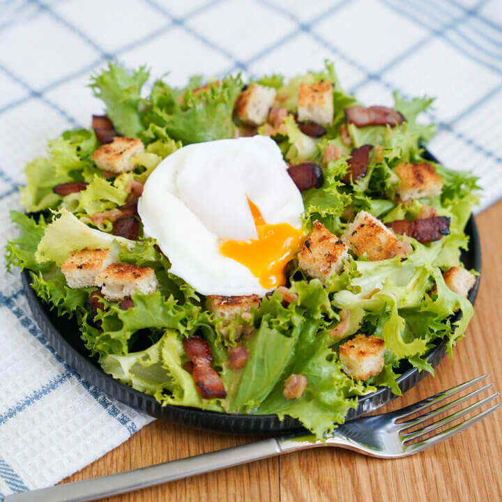 plate of salade lyonnaise, lyonnaise salad, with fork below plate.