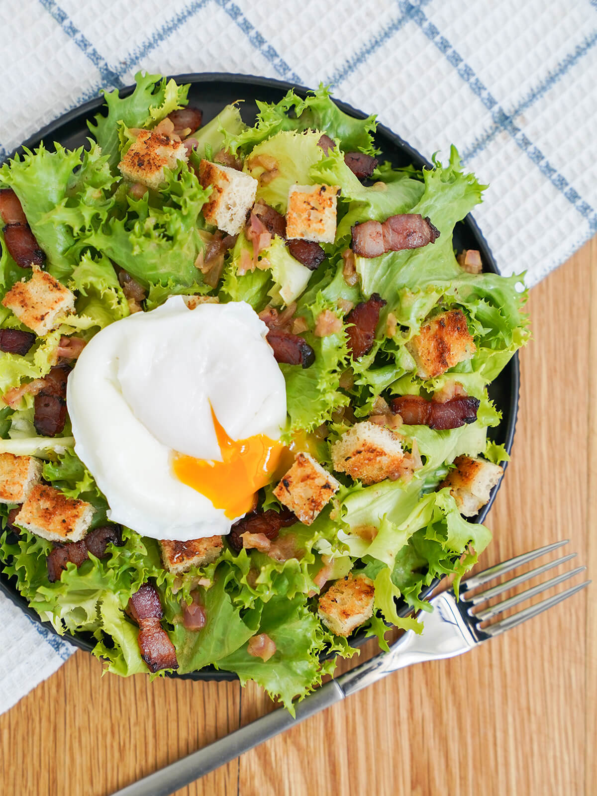 overhead view of a plate of salade lyonnaise from overhead with fork below plate.