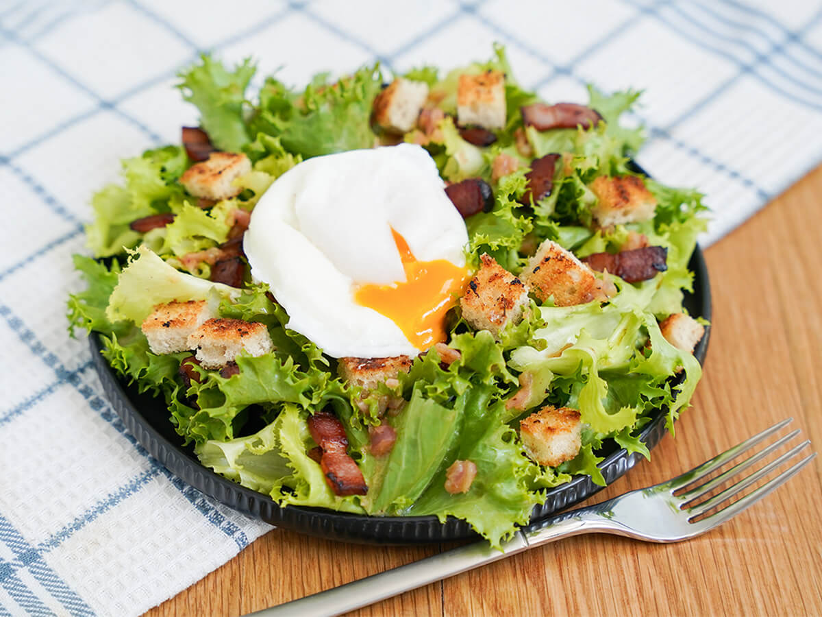 side view of a plate of salade lyonnaise with egg yolk bleeding into salad.