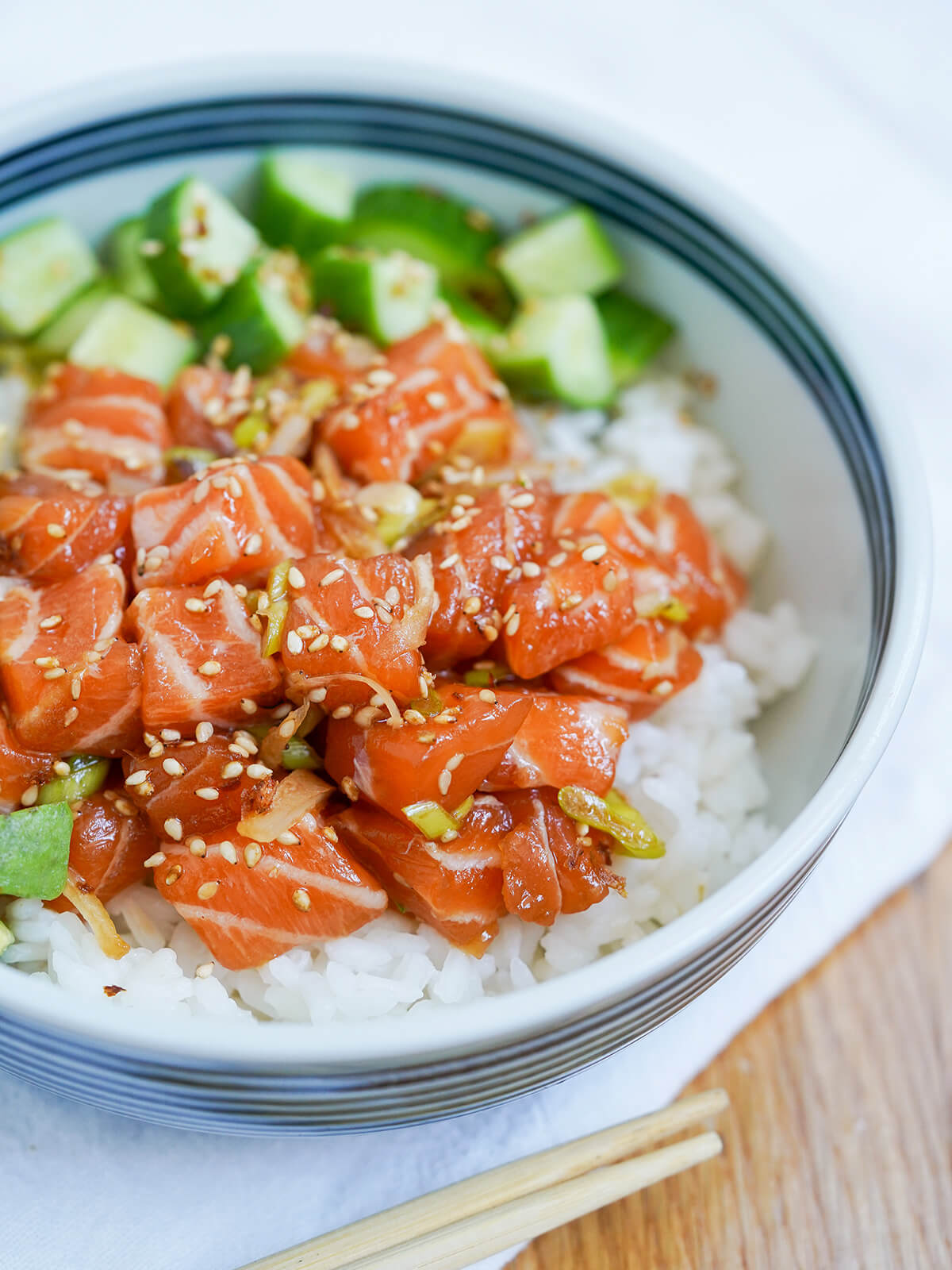 side part view of salmon poke over rice in bowl with chopsticks below