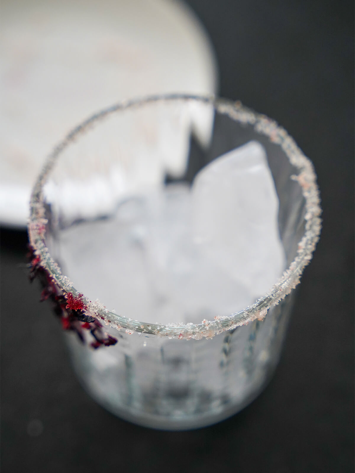 glass rimmed with salt and with some cut hibiscus on side and ice in glass.
